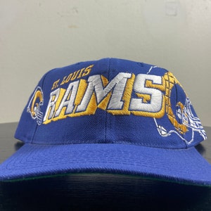 May include: A blue baseball cap with the words "St. Louis Rams" embroidered in white and gold. The cap has a green underbrim.