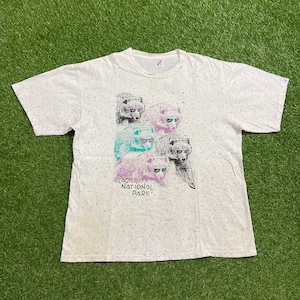 May include: White t-shirt with a tie-dye effect and a graphic of four bears wearing sunglasses. The text "Glacier National Park" is printed below the bears.