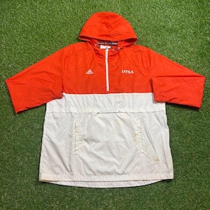 May include: Orange and white Adidas hooded anorak jacket. The top half is orange, the bottom half is white, and it has a white zip. The word "UTSA" is printed on the right chest.
