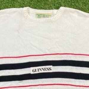 May include: White long-sleeve sweater with red and black stripes and a white label with the text "GUINNESS" in black.