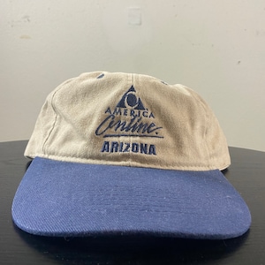 May include: A tan and blue baseball cap with the logo "America Online" and the text "Arizona" embroidered on the front.