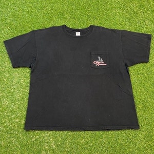 以下が含まれることがあります： 左側にポケットが付いた黒色の半袖Tシャツ。ポケットには、鷲の刺繍と「Original America」の文字が刺繍されています。