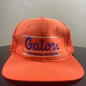May include: An orange baseball cap with a white and purple embroidered logo that reads "Gators University of Florida".