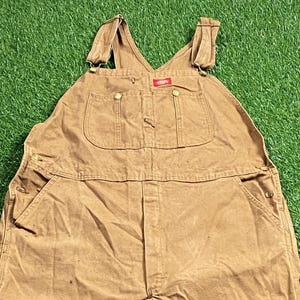 以下が含まれることがあります： 調節可能なストラップと単一の胸ポケットが付いた茶色のキャンバスオーバーオール。オーバーオールは使い古した外観で、耐久性のある素材で作られています。