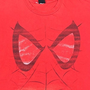 Puede incluir: Camiseta roja con un gr&aacute;fico en blanco y negro de los ojos y el dise&ntilde;o de la telara&ntilde;a de Spider-Man.