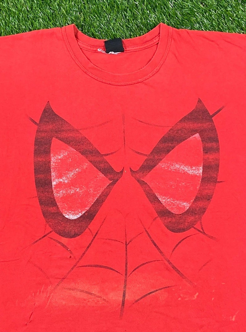 Puede incluir: Camiseta roja con un gr&aacute;fico en blanco y negro de los ojos y el dise&ntilde;o de la telara&ntilde;a de Spider-Man.