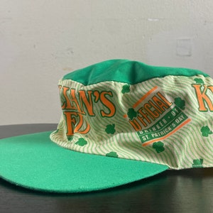 May include: Green and white baseball cap with the text "Killian's Irish Red" and "Official Drinker of St. Patrick's Day" in orange and white.