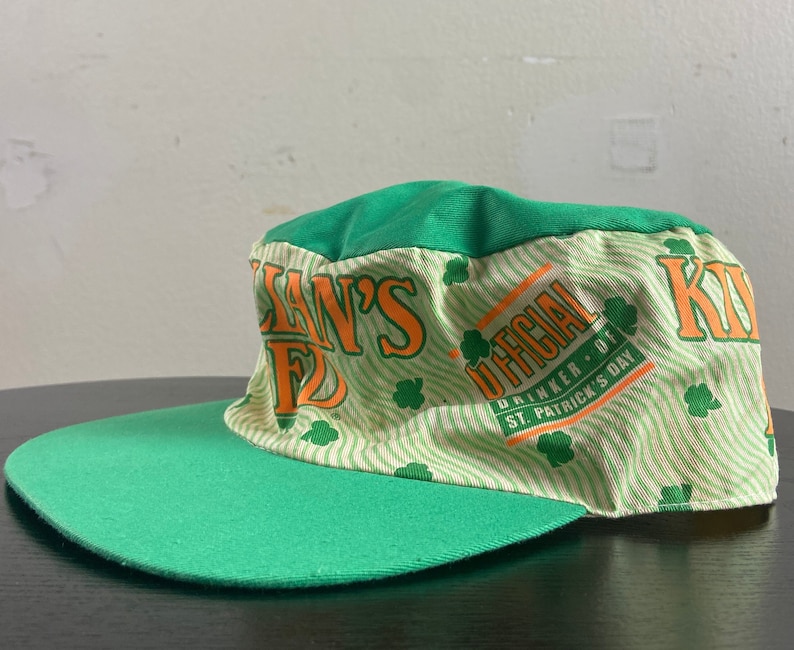 May include: Green and white baseball cap with the text "Killian's Irish Red" and "Official Drinker of St. Patrick's Day" in orange and white.
