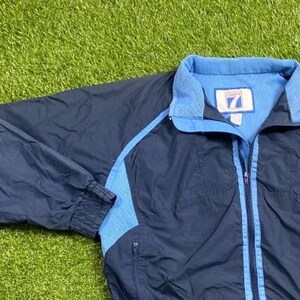 Peut inclure: Une veste coupe-vent bleu marine avec des accents bleu clair et un logo Carolina Tar Heels sur le c&ocirc;t&eacute; droit. La veste a une fermeture &eacute;clair et deux poches.