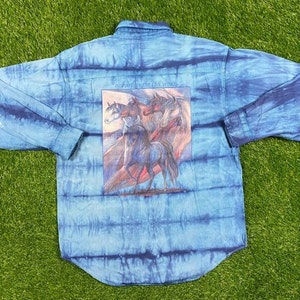 Könnte beinhalten: Ein blaues, tie-dye-farbenes Hemd mit langen Ärmeln und Knöpfen, auf dem Rücken ein Motiv mit Pferden. Das Motiv lautet "In Harmonie mit den vier Winden".