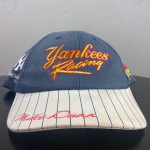 May include: A navy blue baseball cap with "Yankees Racing" embroidered in yellow and red script. The brim is white with navy pinstripes and the name "Mike Dunn" in red script. The cap features the Yankees logo.