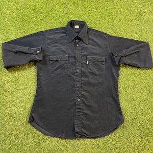 Puede incluir: Una camisa negra de manga larga con botones, dos bolsillos en el pecho y un solo botón en el puño.