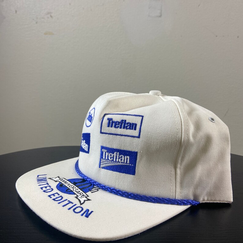 May include: White baseball cap with blue embroidered logos, including "Treflan" and "20th Anniversary Limited Edition".