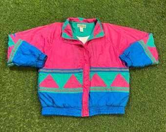 May include: A pink, blue, and green windbreaker jacket with a geometric pattern. The jacket has a zipper closure and a drawstring hood.