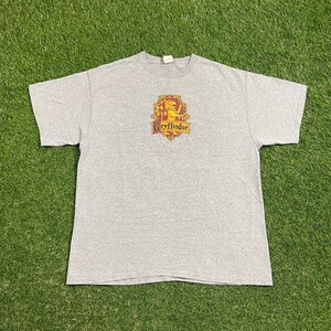 May include: A gray t-shirt with a Gryffindor crest featuring a lion, a red and gold shield, and the text "Gryffindor".