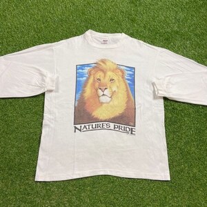 May include: White long-sleeve t-shirt with a graphic of a lion's head against a blue sky. The text "NATURE'S PRIDE" is printed below the image.
