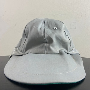 May include: A grey baseball cap with a wide brim and a green underside. The cap has two white eyelets on top.