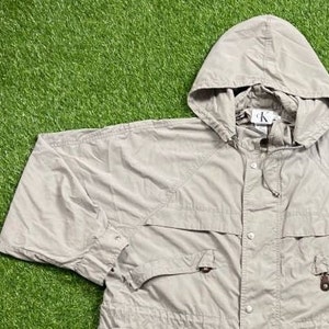 Pu&ograve; includere: Giacca con cappuccio color beige chiaro con coulisse e chiusura con bottoni. La giacca ha due tasche frontali e un piccolo logo sul cappuccio. La giacca &egrave; realizzata in materiale leggero.