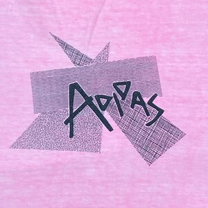 Peut inclure: Un t-shirt rose avec un motif graphique noir du mot "Adidas" dans un design g&eacute;om&eacute;trique.