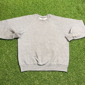 May include: A grey crew neck sweatshirt with long sleeves. The sweatshirt features ribbed cuffs and a ribbed hem. The garment is made of a soft, comfortable material.