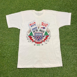 以下が含まれることがあります： スーパーボウルXXVのグラフィックが特徴のオフホワイトのヴィンテージTシャツ。デザインには「Super Bowl XXV」と「Giants」と「Bills」の文字、フットボールフィールドと星のアクセントが含まれています。シャツは柔らかい素材で作られています。