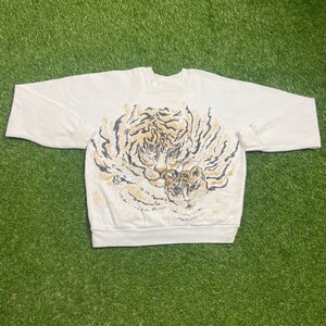 May include: White sweatshirt with a graphic print of two tigers. The larger tiger is in the center of the print and the smaller tiger is nestled in the larger tiger's fur. Both tigers are brown and black.