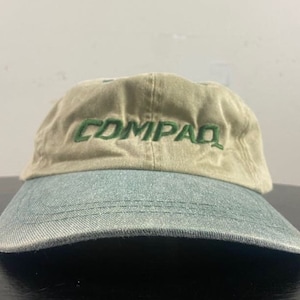 May include: A tan and green baseball cap with the word "COMPAQ" embroidered in green on the front.