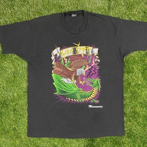 May include: Black t-shirt with a graphic print of a green dragon and a golden eagle fighting. The text "Wild Spirit" is printed above the graphic. The text "Minnesota" is printed below the graphic.