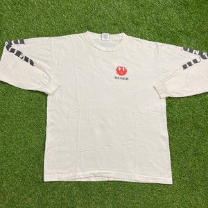 K&ouml;nnte beinhalten: Wei&szlig;es Langarm-T-Shirt mit einem roten Ruger-Logo und schwarzem Text auf den &Auml;rmeln, der "Ruger" lautet.