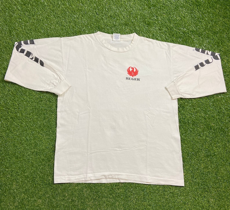 K&ouml;nnte beinhalten: Wei&szlig;es Langarm-T-Shirt mit einem roten Ruger-Logo und schwarzem Text auf den &Auml;rmeln, der "Ruger" lautet.
