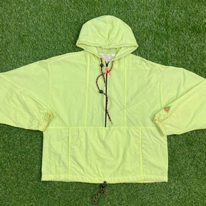 May include: A bright yellow hooded anorak jacket with a black zipper and drawstring. The jacket has a kangaroo pocket and a small logo on the sleeve.