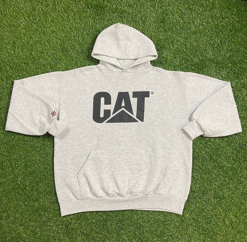 May include: A gray hooded sweatshirt with a black CAT logo on the front. The logo is a stylized black cat with the word CAT above it.