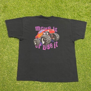 Może przedstawiać: Czarny T-shirt z grafiką czerwonego monster trucka z napisem "Move it or Lose it" nadrukowanym na fioletowo.