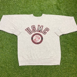 May include: A gray sweatshirt with a red and black USMC logo. The logo includes the words "United States Marine Corps".