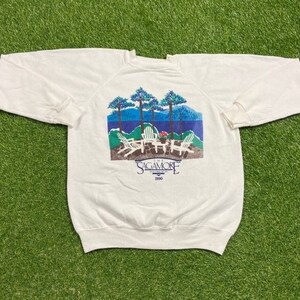 May include: White sweatshirt with a colorful graphic of trees, a lake, and chairs. The graphic says "The Sagamore 1990".