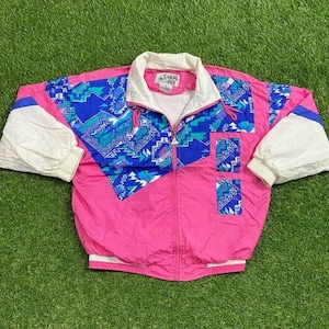 May include: A pink, white, and blue windbreaker jacket with a geometric pattern. The jacket has a zipper closure and a stand-up collar. The brand name "Casual Isle" is printed on the zipper pull.
