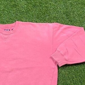 May include: A pink crew neck sweatshirt with a ribbed neckline and cuffs. The sweatshirt is made of a soft, comfortable fabric.