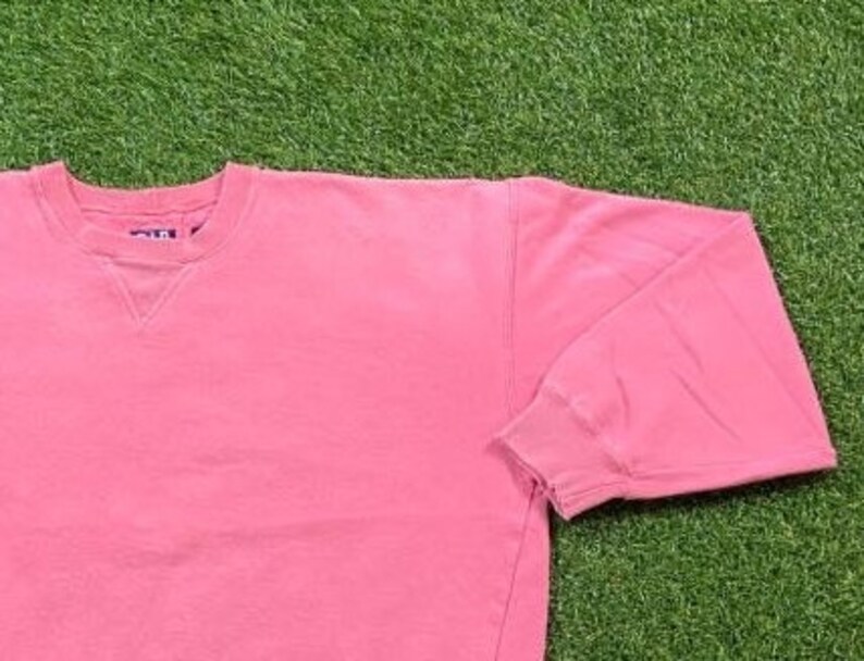 May include: A pink crew neck sweatshirt with a ribbed neckline and cuffs. The sweatshirt is made of a soft, comfortable fabric.