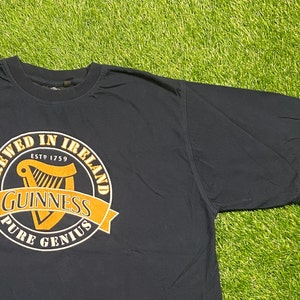 May include: A black t-shirt with a yellow and white Guinness logo. The logo says "Brewed in Ireland Est 1759 Guinness Pure Genius".
