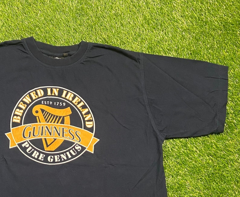 May include: A black t-shirt with a yellow and white Guinness logo. The logo says "Brewed in Ireland Est 1759 Guinness Pure Genius".