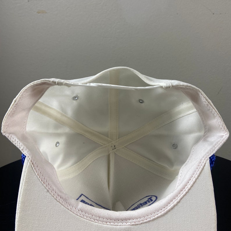 May include: White baseball cap with a blue mesh back and a white adjustable strap. The inside of the cap is white with a blue label that says "The Original"