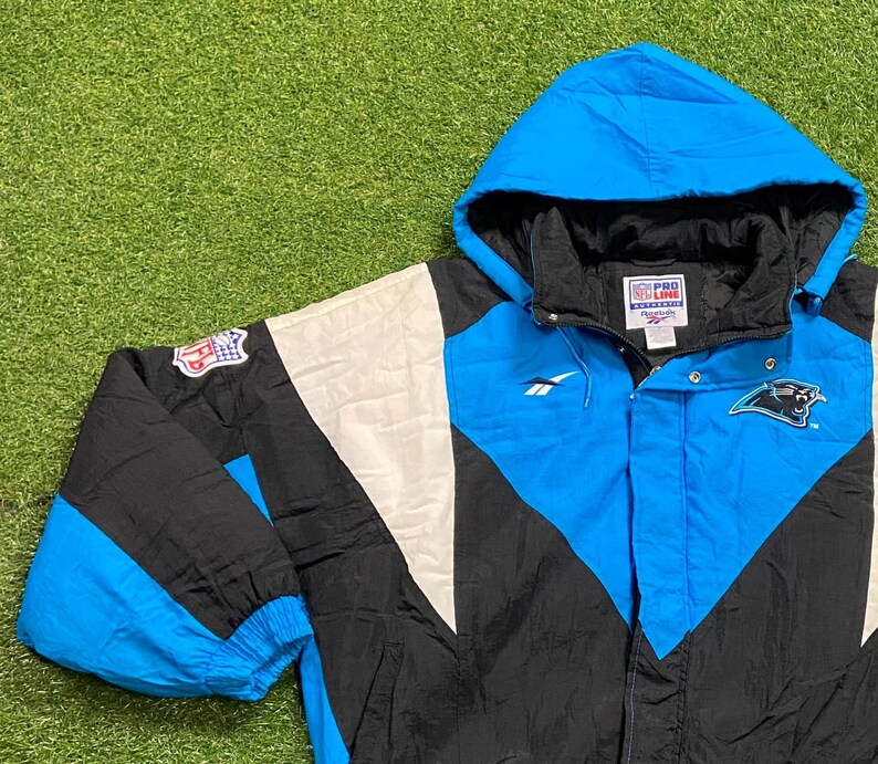 Peut inclure: Veste &agrave; capuche des Carolina Panthers en noir, blanc et bleu. La veste pr&eacute;sente le logo de l'&eacute;quipe, le logo NFL et la marque Reebok. Fermeture &eacute;clair compl&egrave;te et capuche.