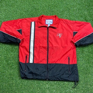 May include: A red and black windbreaker jacket with a white stripe down the front and a Buccaneers logo on the chest. The jacket has a zip closure and two pockets.