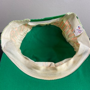 May include: Green and white baseball cap with a white strap and a "Designer Pro" label. The cap has a green brim and a white crown with a green and white pattern.