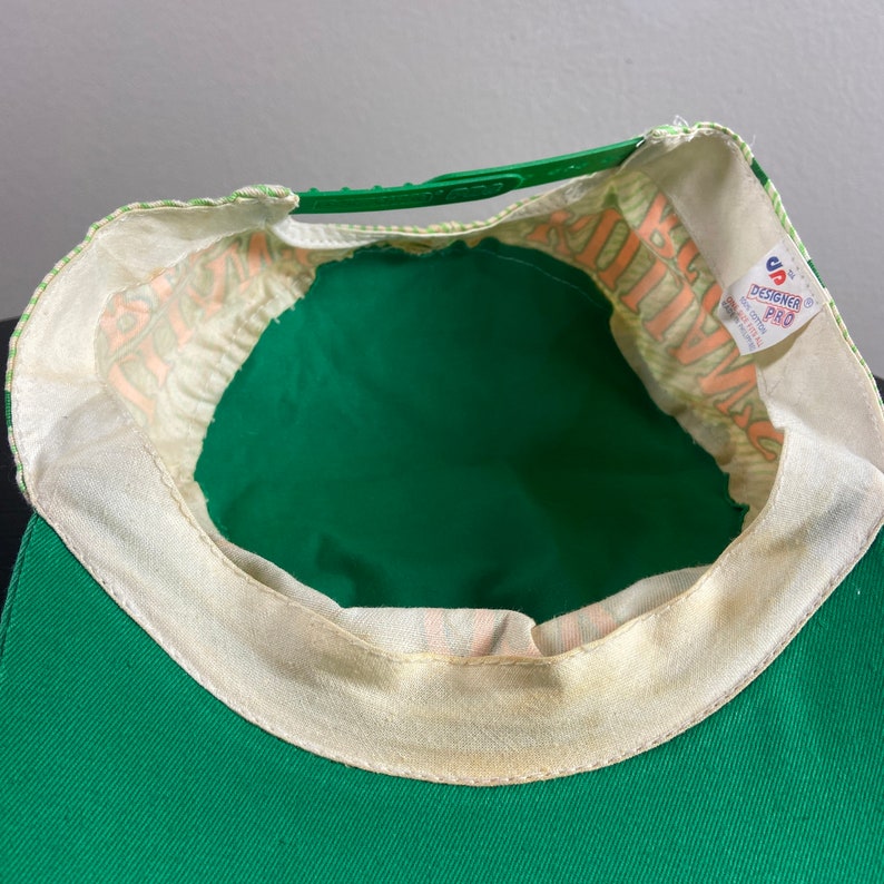 May include: Green and white baseball cap with a white strap and a "Designer Pro" label. The cap has a green brim and a white crown with a green and white pattern.