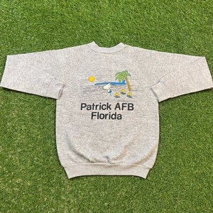 May include: A gray sweatshirt with a graphic of Snoopy surfing with the text "Patrick AFB Florida" printed on the front.