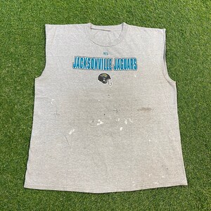 May include: A gray sleeveless t-shirt with the text "NFL Jacksonville Jaguars" in blue and teal lettering. A teal and black football helmet graphic is below the text.
