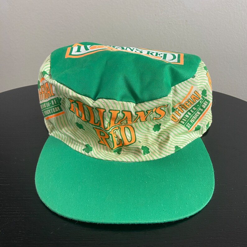 May include: Green and white baseball cap with the text "O'Dallan's Red" and "Official Drinker - St. Patrick's Day" printed on it.