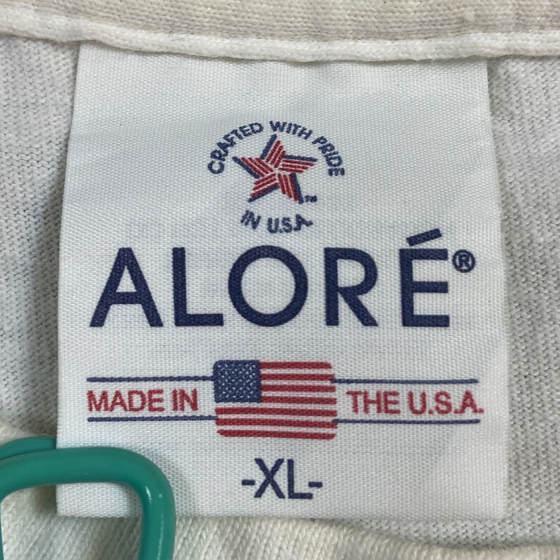 K&ouml;nnte beinhalten: Wei&szlig;es Etikett mit blauem Text, der "Crafted with Pride" und "ALORE&reg;" lautet, mit einem Stern und den Worten "in USA" &uuml;ber dem Markennamen. Unter dem Markennamen befindet sich eine kleine amerikanische Flagge und der Text "Made in the U.S.A." und "XL".