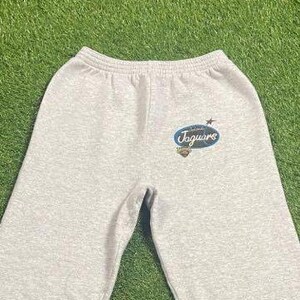 May include: Light gray sweatpants with an elastic waistband. The sweatpants feature a blue and white logo that says "Jaguars" with a star and shield design. The pants are made of a soft, comfortable material.